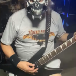 The Hellion Emerges. Masked up. Plugged in. Hellion in its natural state. Guitarist wearing a Hellion mask and Hellion t-shirt playing guitar in a recording studio.